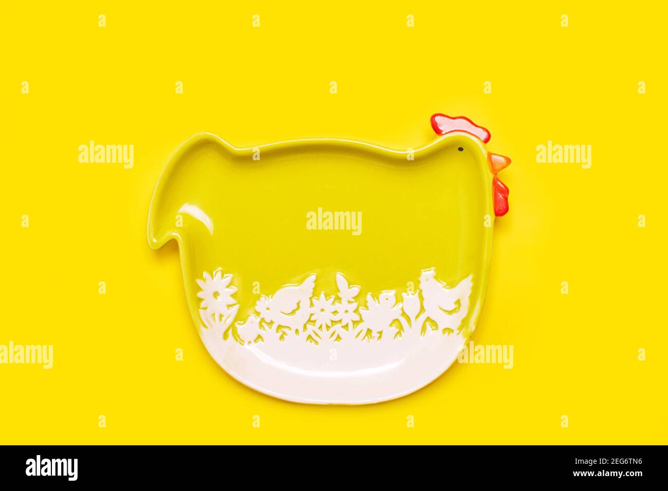 Simple easter frame background with green funny hen plate over bright yellow color, flat lay