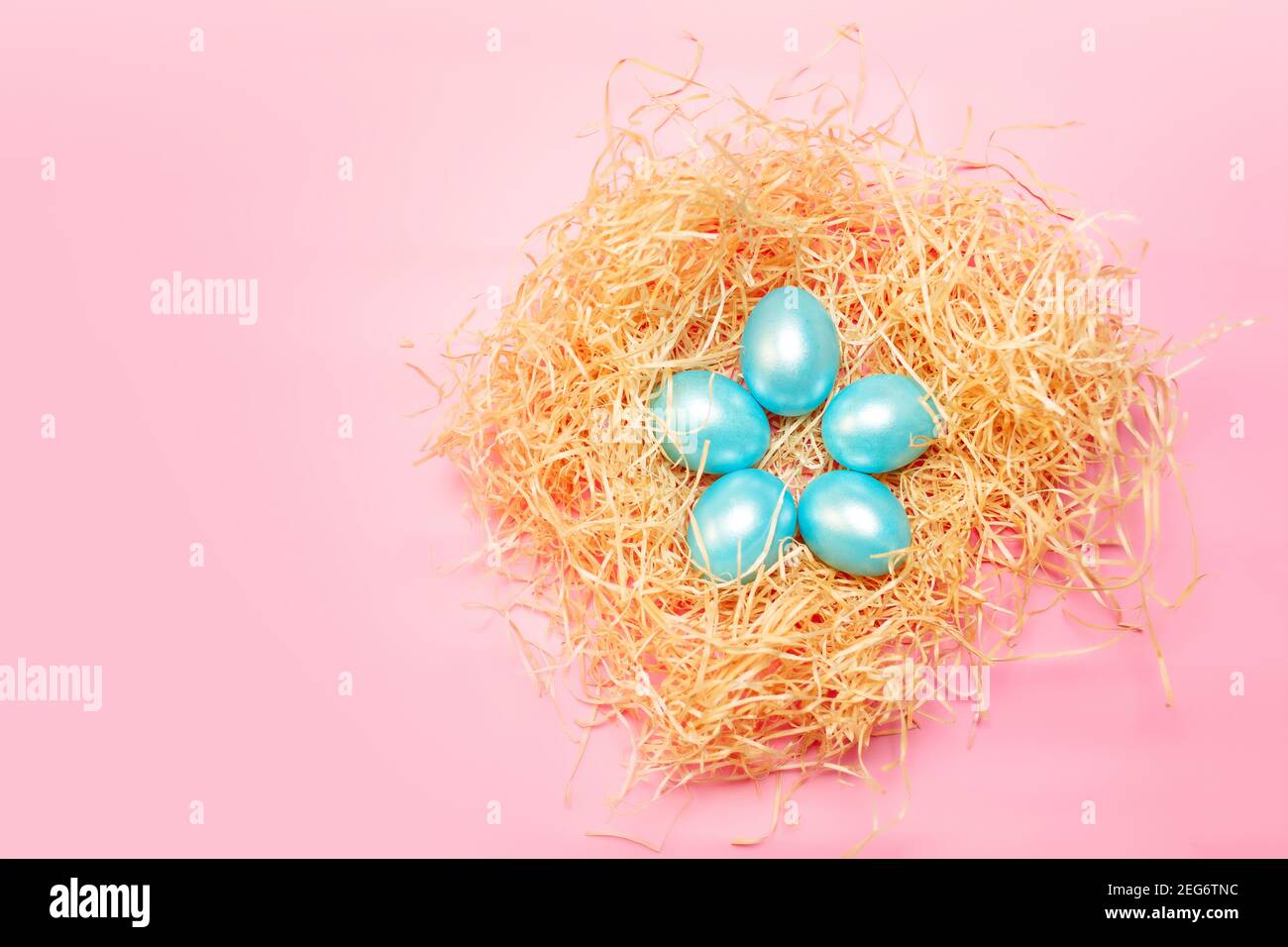 Happy easter simple background, colored pearl blue eggs in hay nest over bright pink color, top view with copy space Stock Photo