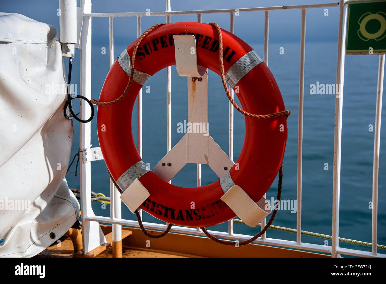 A red lifebuoy hangs on the rail of a boat on the open sea - ready to help people in distress - in the background you can see the deep blue sea on a b Stock Photo