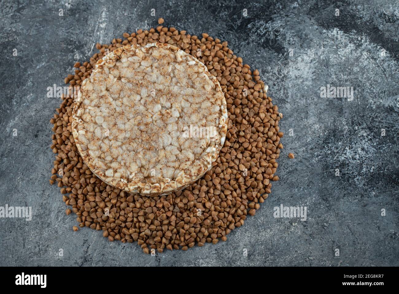 Single rice cake and uncooked buckwheat on marble surface Stock Photo