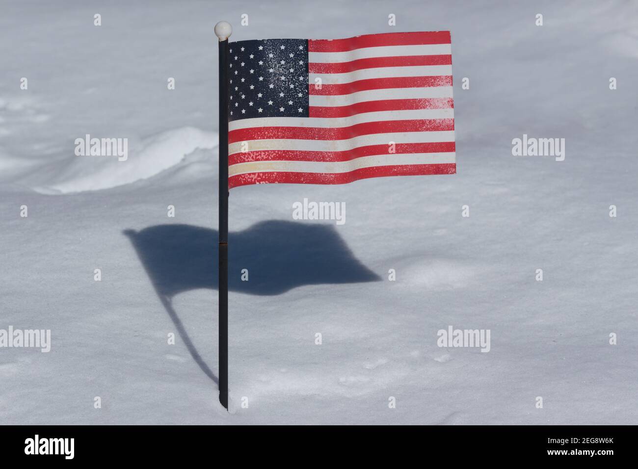 an American flag planted in a snow covered ground on a very sunny day with a strong cast shadow behind it Stock Photo
