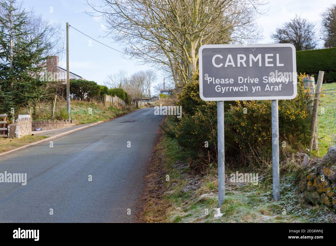 Carmel, Flintshire; UK: Feb 11, 2021: A place name sign at the entrance to the village of Carmel incorporates a bilingual Welsh and English message wh Stock Photo