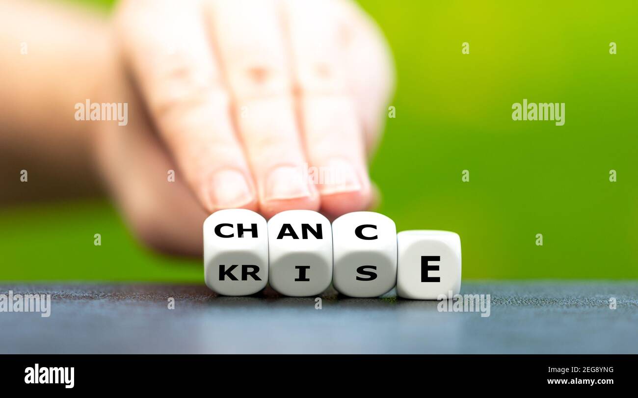 Hand turns dice and changes the German word 'Krise' (crisis) to 'Chance' (chance). Stock Photo