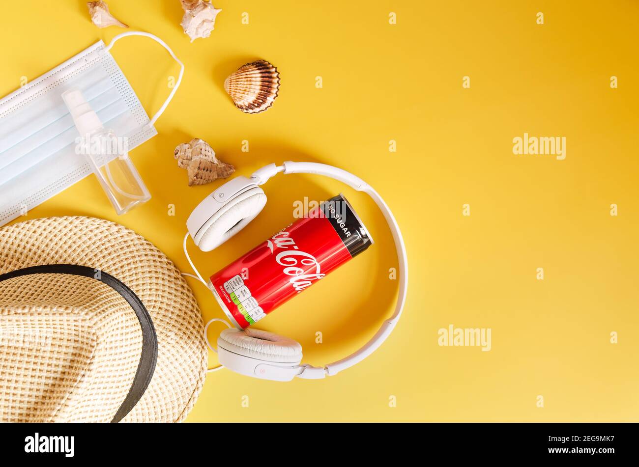 Travel under Covid-19 and new normal concepts. Top view of white headphones, can of Coca- Cola, phone and beach hat on yellow background close up Stock Photo
