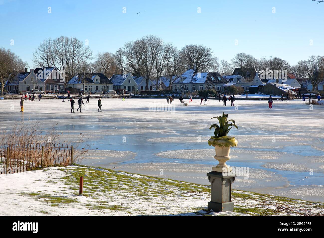 Winter snow and people ice skating on frozen water in Broek in Waterland, a small town with traditional old and painted wooden houses, North Holland, Stock Photo