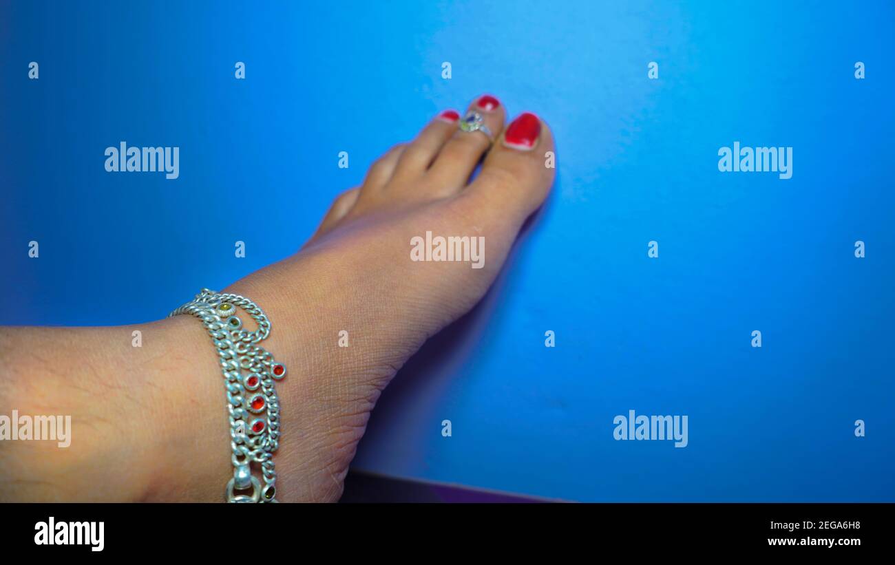 The traditional Hindu woman bride wearing paajeb (Anklets) in India. Female foot with Nail polish isolated on blue background Stock Photo