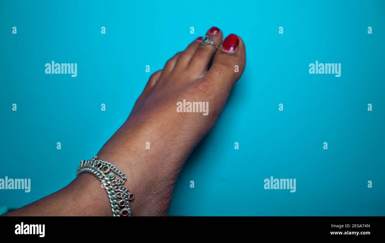 The traditional Hindu woman bride wearing paajeb (Anklets) in India. Female foot with Nail polish isolated on blue background Stock Photo
