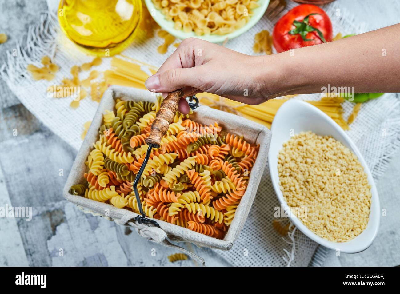 Hand holding a basket of raw fusilli pasta with assorted pasta and