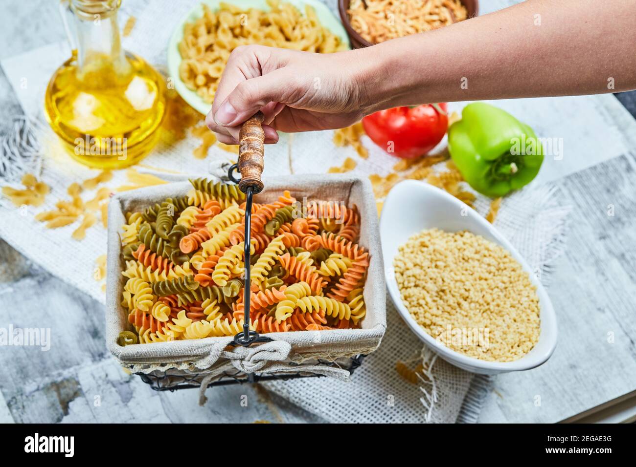 Hand holding a basket of raw fusilli pasta with assorted pasta and