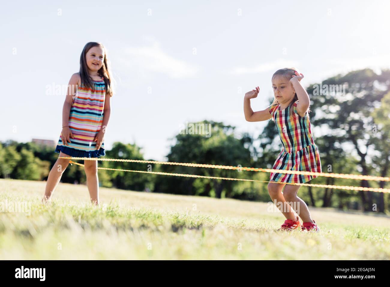 Two girls playing Chinese jumping rope in the park. Childhood games. Stock Photo