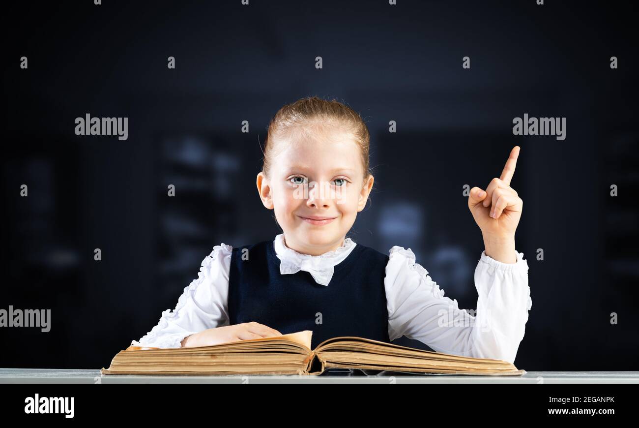 Smiling little girl sitting at desk with open book Stock Photo - Alamy