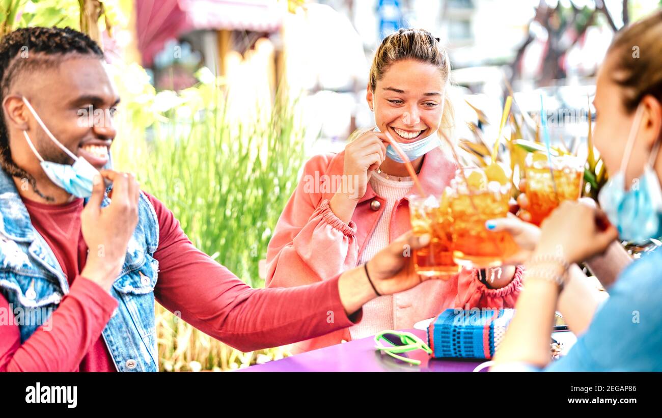 Young people drinking at cocktail bar with open face mask - New normal friendship concept with happy friends having fun together toasting drinks Stock Photo