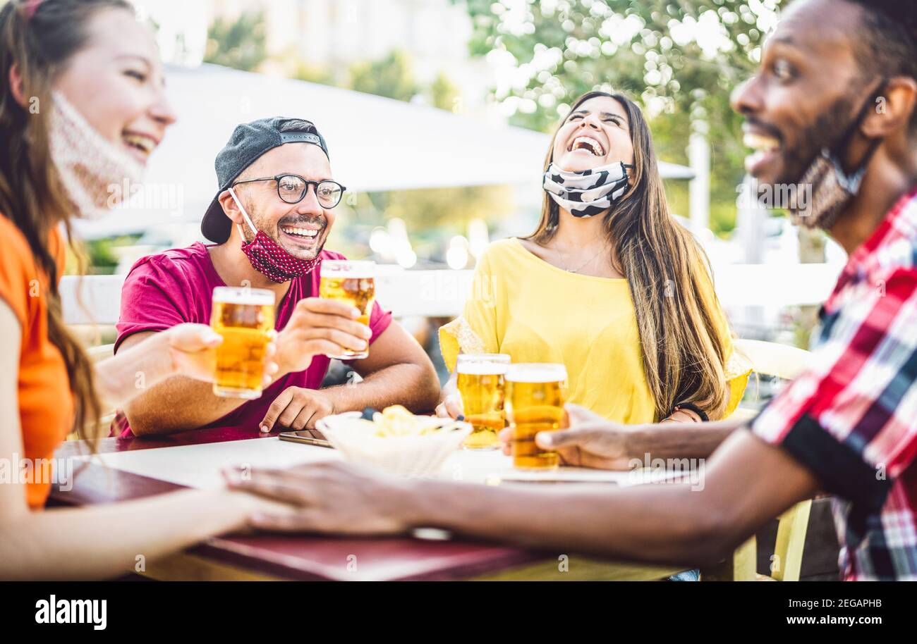 Young people drinking beer with open face masks - New normal lifestyle concept with friend having fun together talking on happy hour at brewery bar Stock Photo