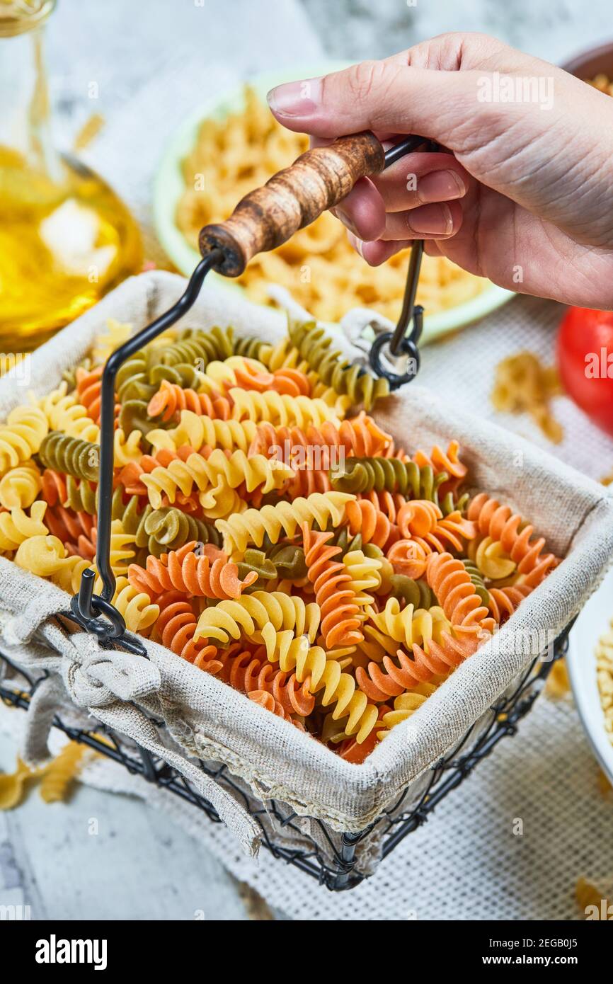 Hand holding a basket of raw fusilli pasta with assorted pasta and