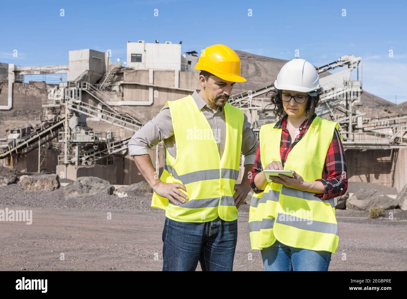 Professional male and female engineers in hardhats and waistcoats checking information on tablet while discussing work issues on construction site Stock Photo