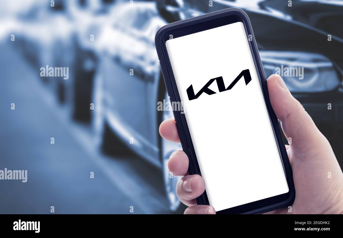 Galicia, Spain; january 09 2021: Hand holding a smart phone with new KIA logo on screen and blurry cars on background. Copy space Stock Photo