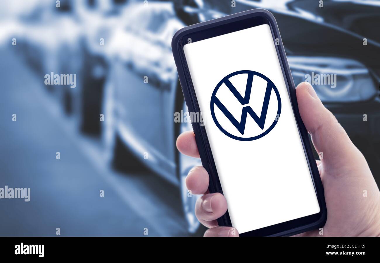 Galicia, Spain; january 09 2021: Hand holding a smart phone with new Volkswagen logo on screen and blurry cars on background. Copy space Stock Photo