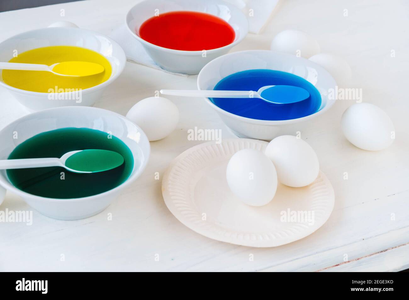 Getting ready for Easter with liquid food coloring. Different colors in different bowls, egds on white table Stock Photo