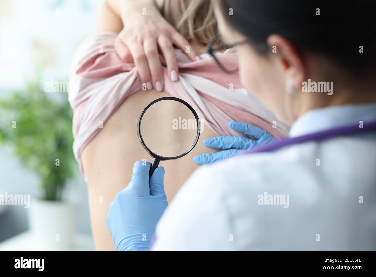 Doctor examining skin on back of female patient using magnifying glass Stock Photo