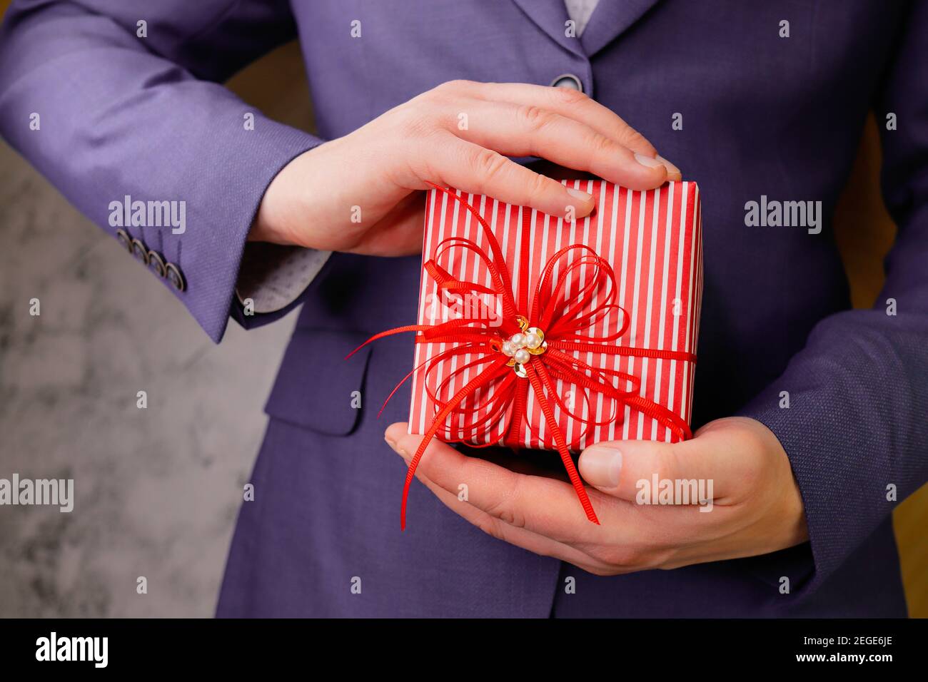 businessman man in blue suit holds gift in two hands. Red box decorated with bow. Stock Photo