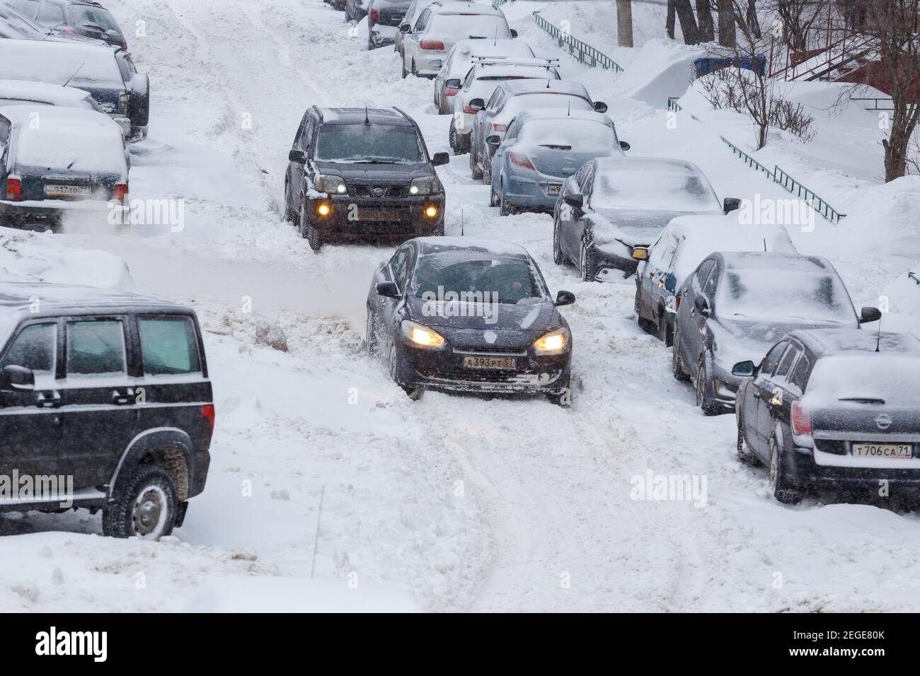 Tula, Russia - February 13, 2021: Two cars drive through a snowy yard between rows of parked cars in deep snow. Stock Photo