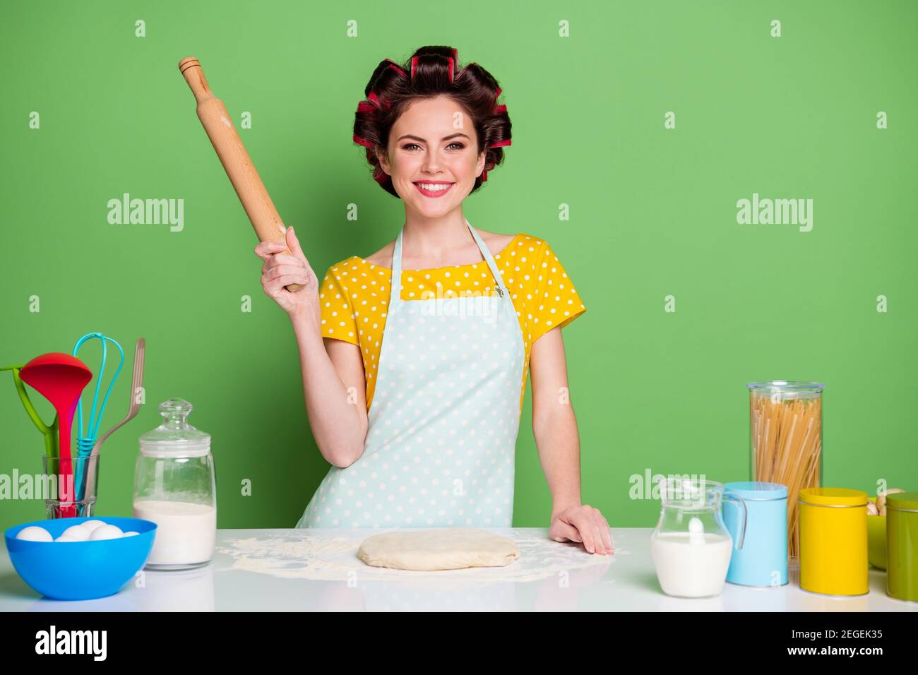 Photo of positive girl hold rolling pin ready knead raw fresh dough for home made cake pie wear yellow dotted t-shirt hair rollers isolated over green Stock Photo