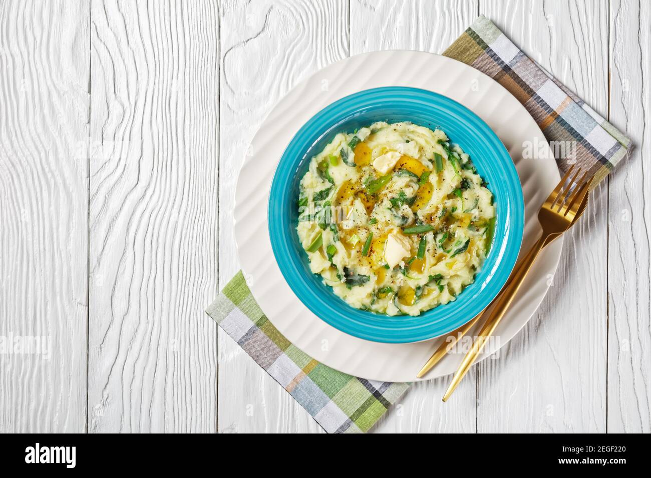 Creamy irish colcannon traditional potato mash with kale, garlic, melted butter and spring onion served on a blue bowl with cutlery on a white wooden Stock Photo