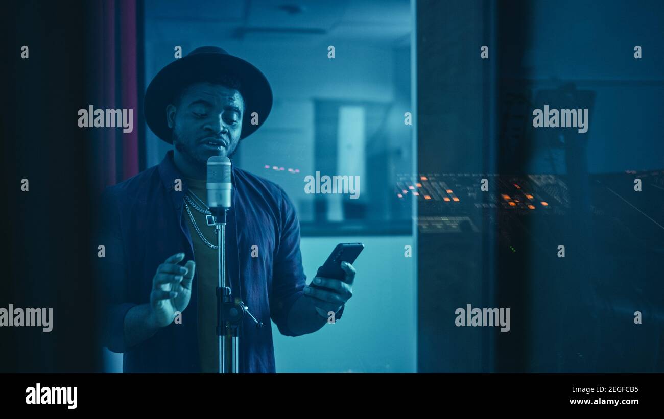 Portrait of Successful Young Black Artist, Singer, Performer Singing His Hit Song for the New Album. Wearing Stylish Hat, Holding Smartphone and Stock Photo