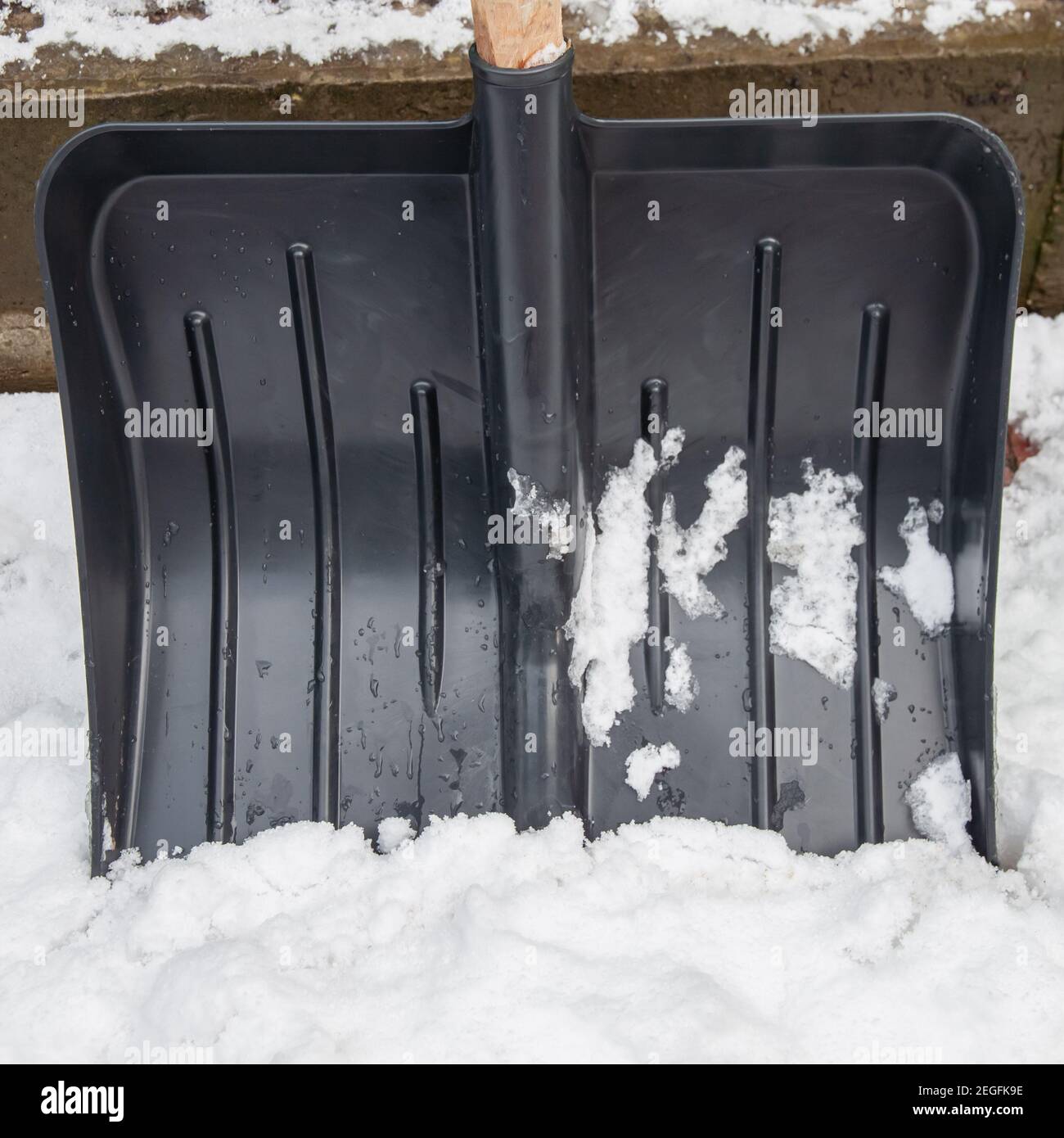 Black plastic snow shovel in the snow closeup. Front view Stock Photo