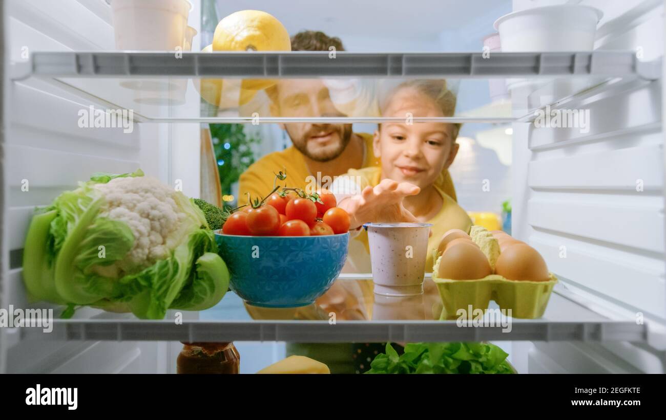 Camera Inside Kitchen Fridge: Dad Lifts Cute Little Daughter to Choose Whatever She wants to Take From the Fridge, She Chooses Healthy Yogurt. Point Stock Photo
