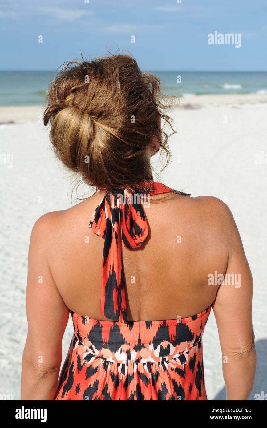 Rear View of a Beautiful Mature Woman Standing on the Beach Weariring a Summer Dress Stock Photo