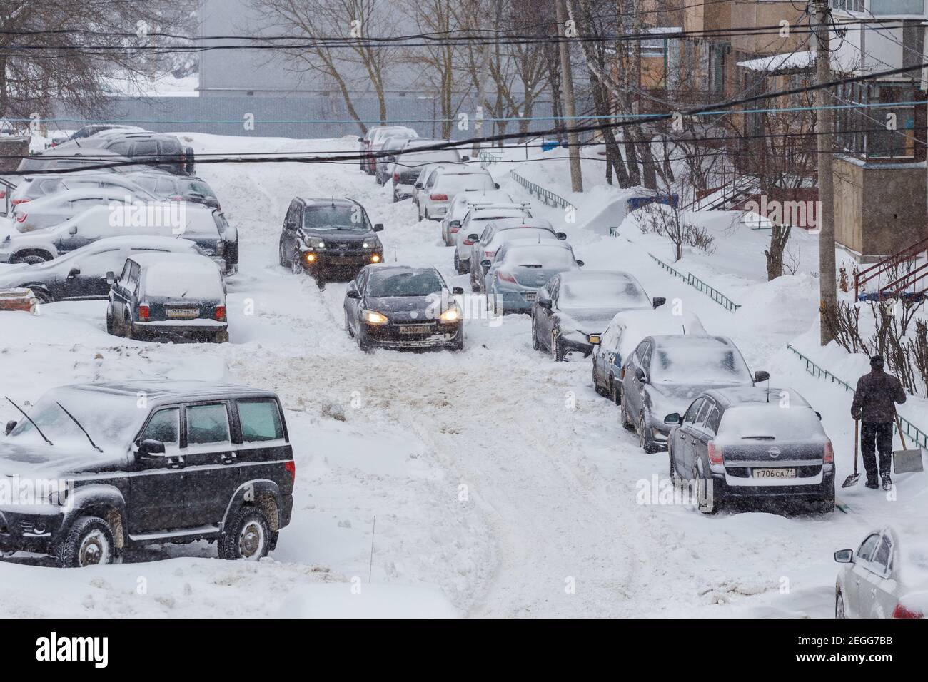 Tula, Russia - February 13, 2021: Two cars drive through a snowy yard between rows of parked cars in deep snow. Stock Photo