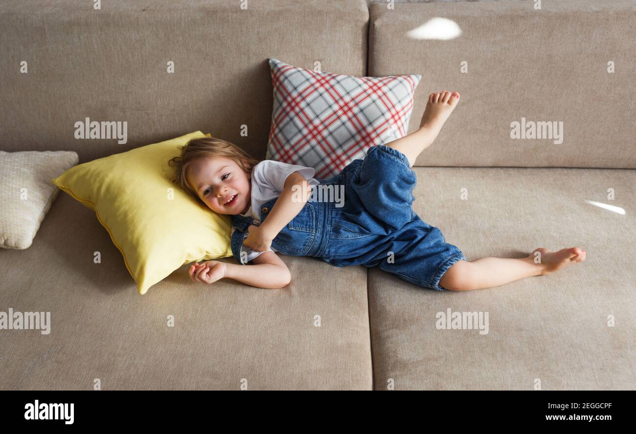a little girl in a blue jumpsuit lies at home on the sofa among the ...