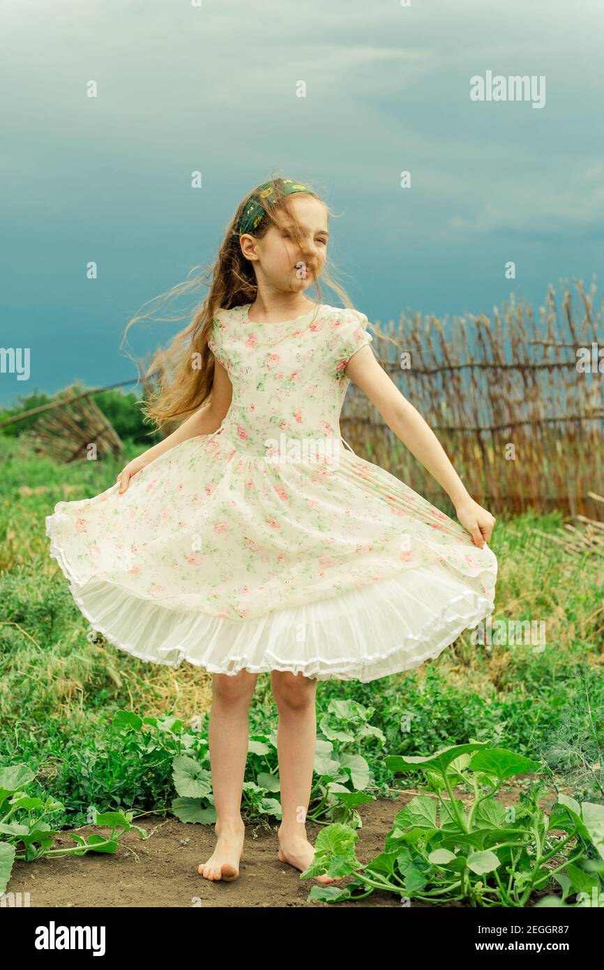 A little girl in a white dress with a flower stands barefoot in the ...