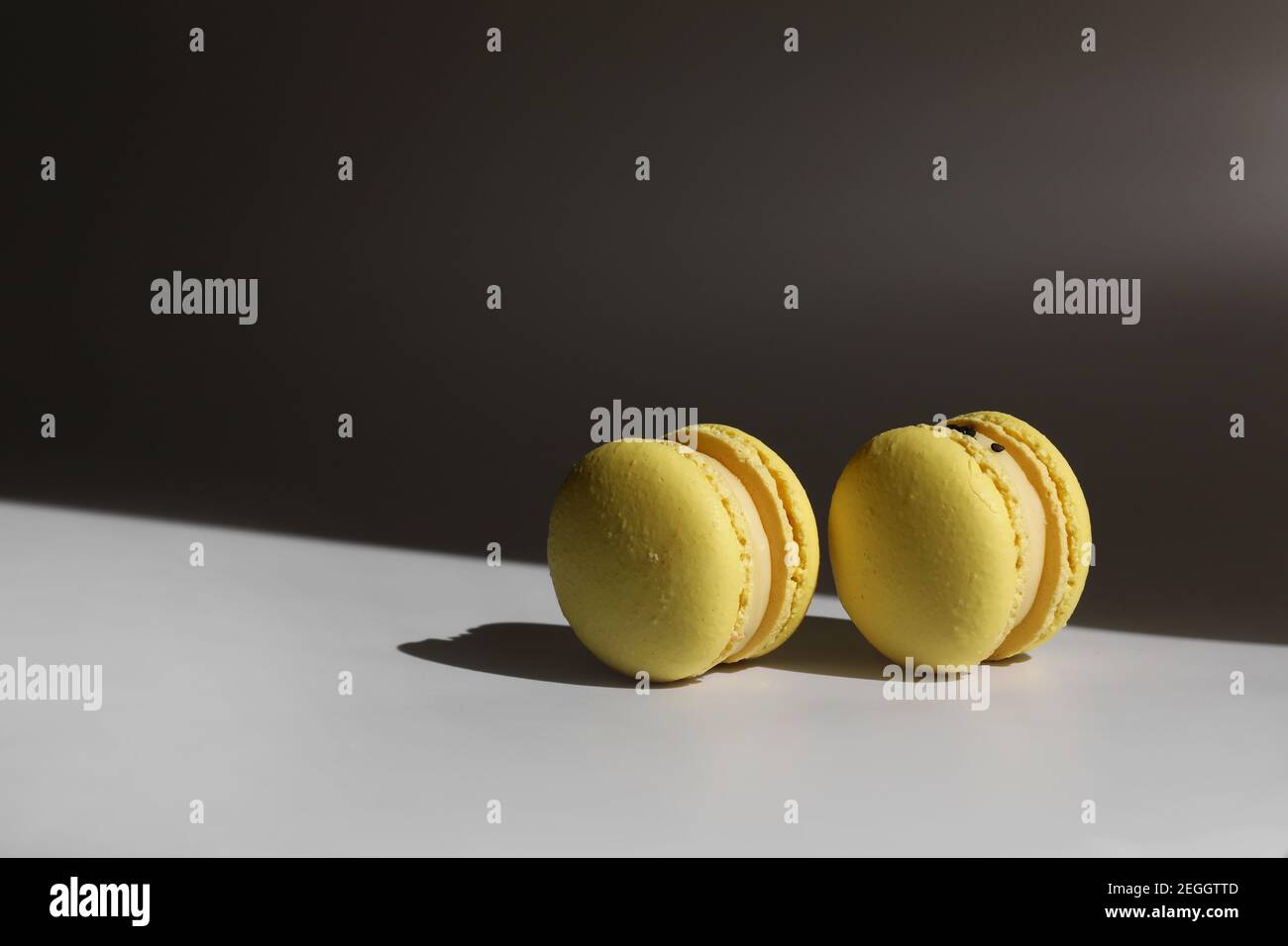 Sweet yellow lemon french macaroons or macarons dessert isolated on white background with light rays from window. Stock Photo