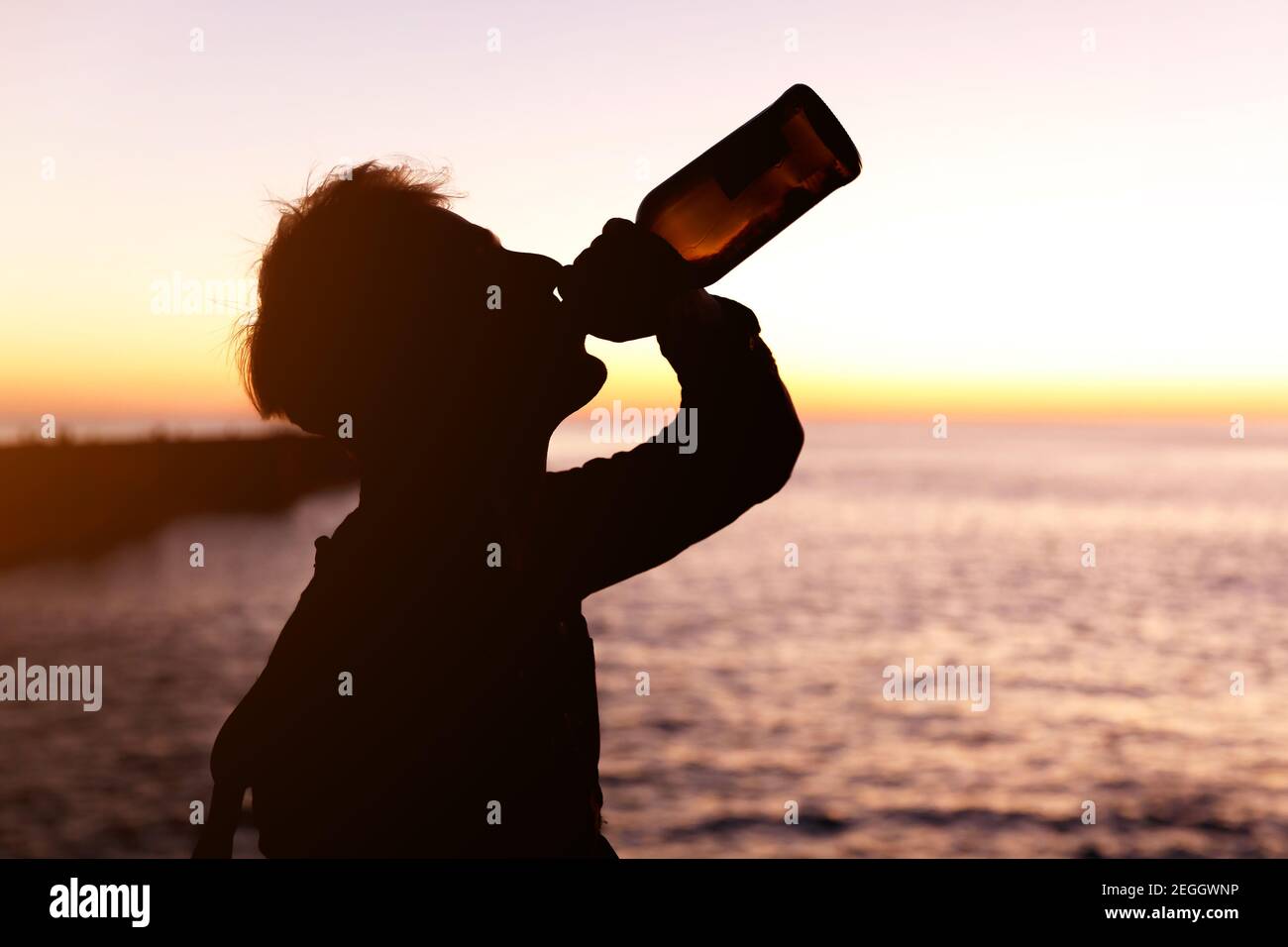 silhouette of young man drinking wine from bottle, ocean and sunset on ...