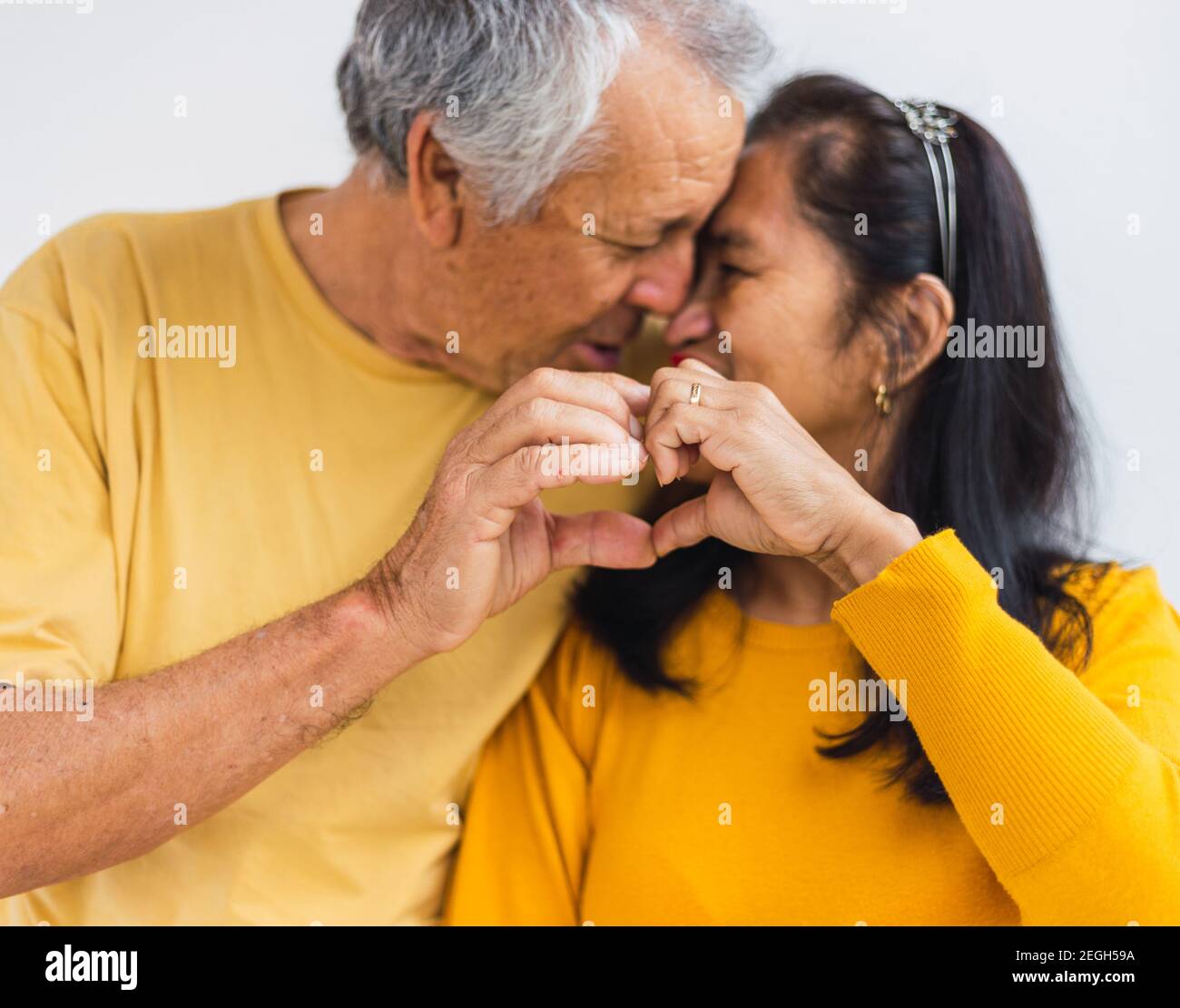 Unrecognizable old couple doing a heart with their hands while kissing Stock Photo