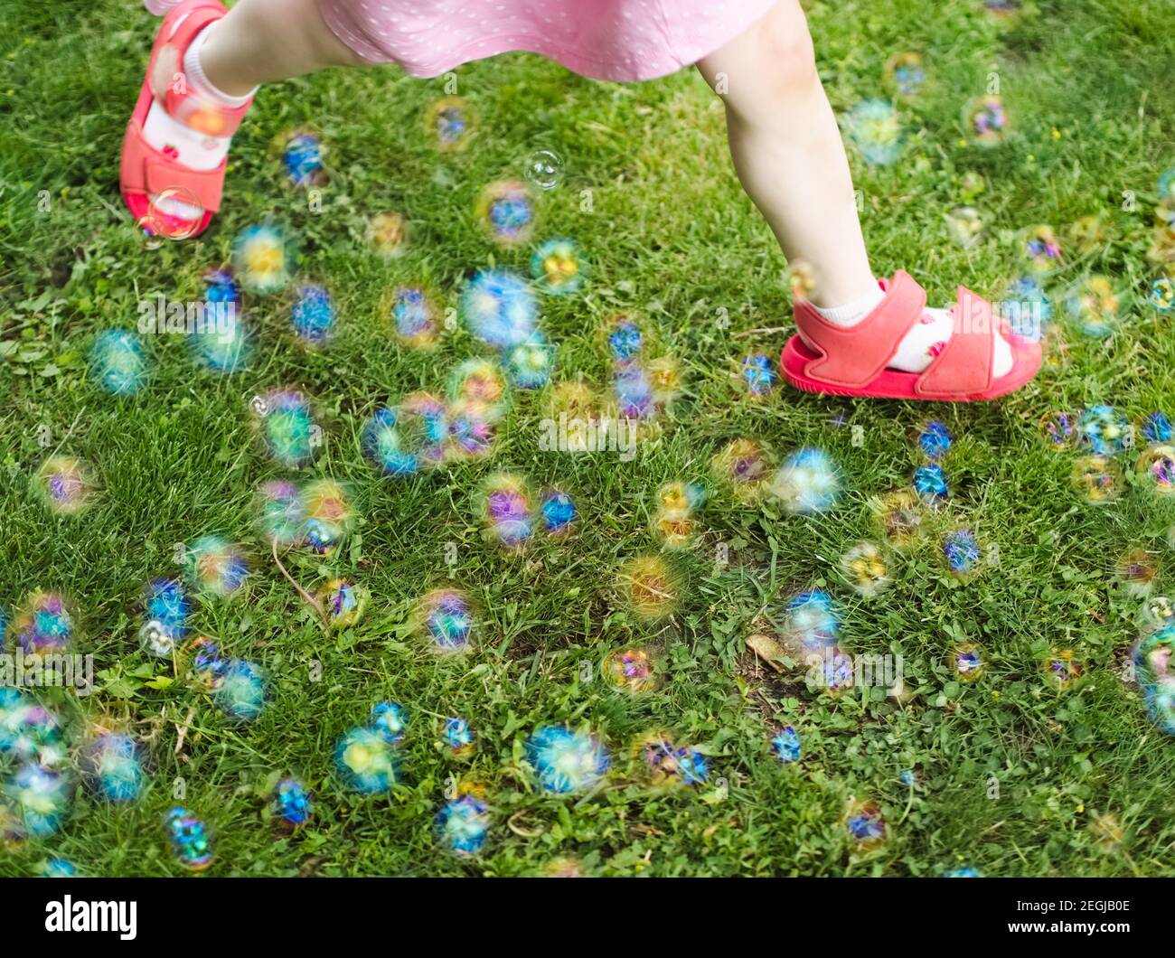 Little Girl in Pink Dress Running Through Soap Bubbles in the Yard Stock Photo