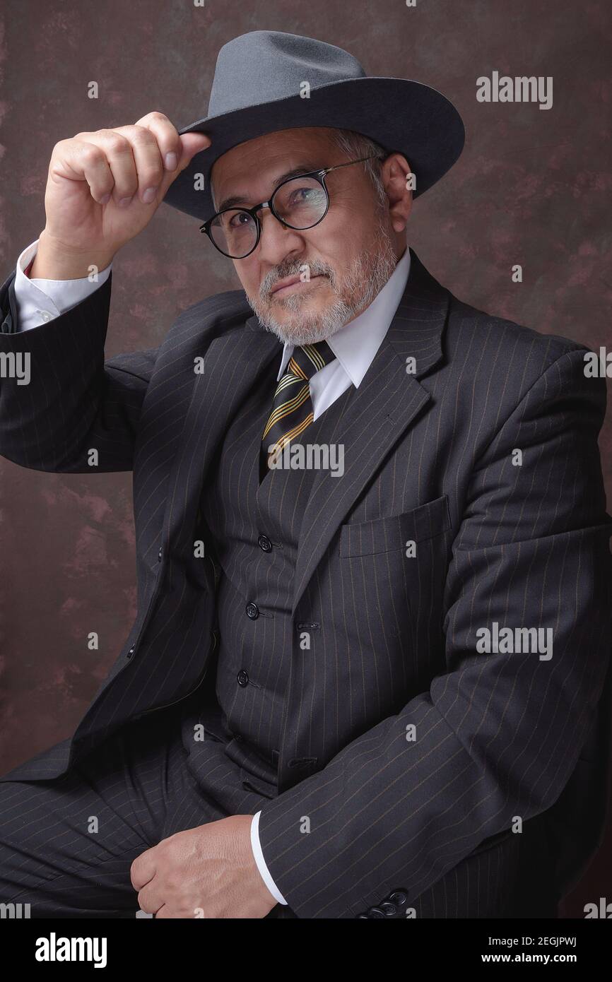A mature gentleman posing for the camera in a dark brown pinstripe suit and hat Stock Photo