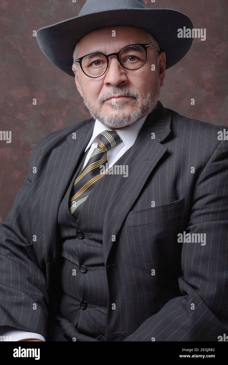 A mature gentleman posing for the camera in a dark brown pinstripe suit and hat Stock Photo