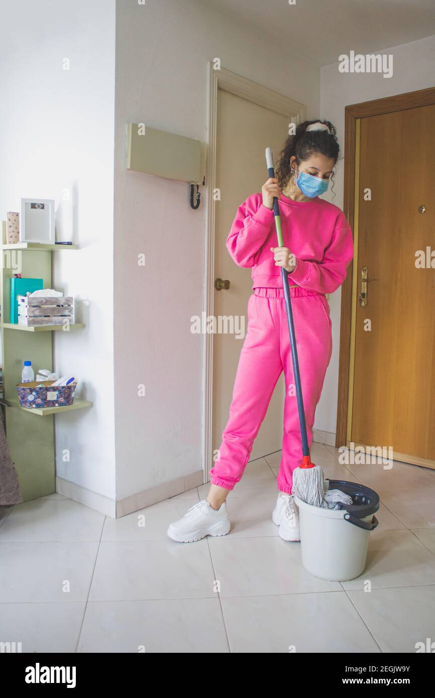 woman mopping the floor of the house with pink tracksuit and mask Stock Photo