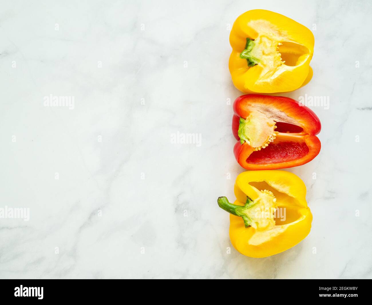 Red and yellow bell peppers sliced by the half with seeds isolated in kitchen counter viewed from above Stock Photo