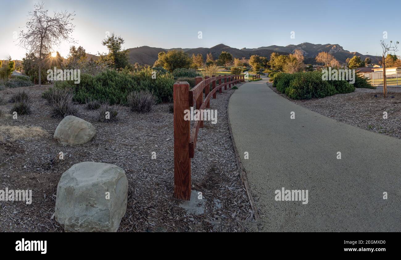 Wooden fence along walking trail of community park guides you through the grassy hills as the sunshine peaks over the mountains. Stock Photo