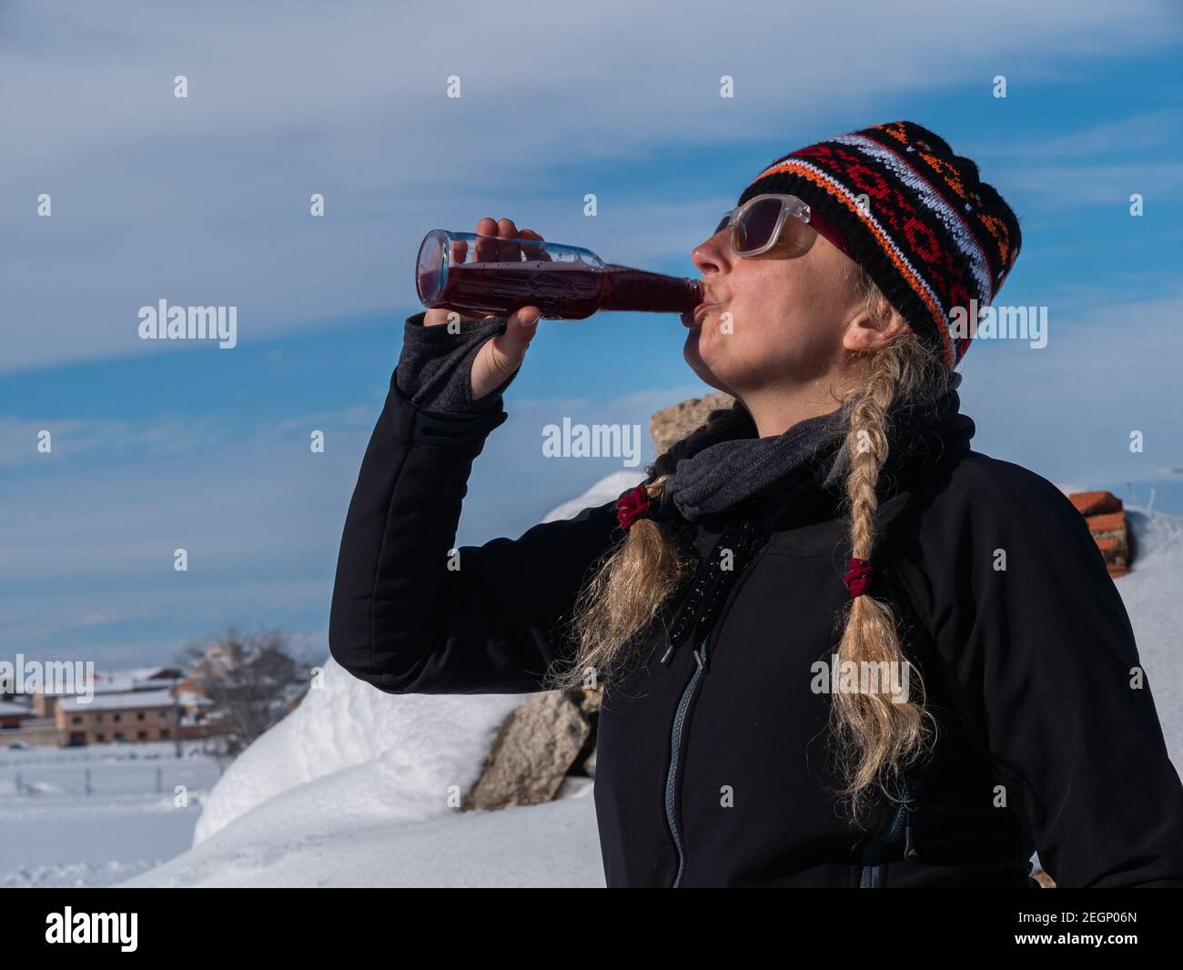 An outdoorsy Caucasian woman in pigtails and winter clothes, drinking soda in a snowy setting Stock Photo