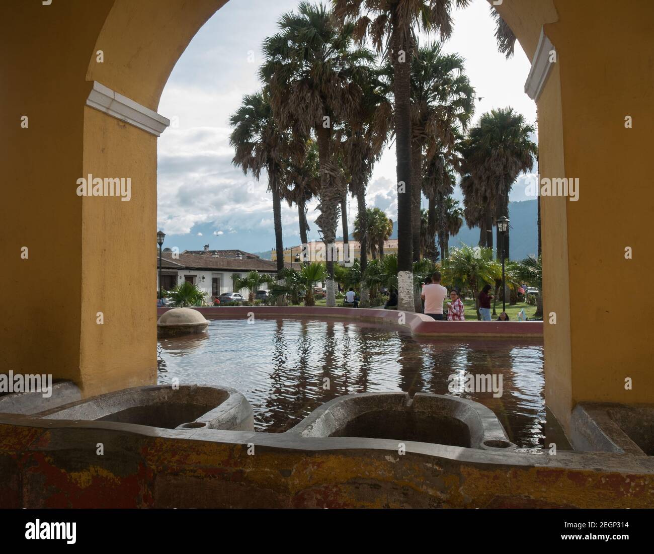 Guatemala, Antigua - May 26, 2019 - Tanque la union public lavoir in the town of Antigua Guatemala, people enjoy near palm trees, yellow walls. Stock Photo