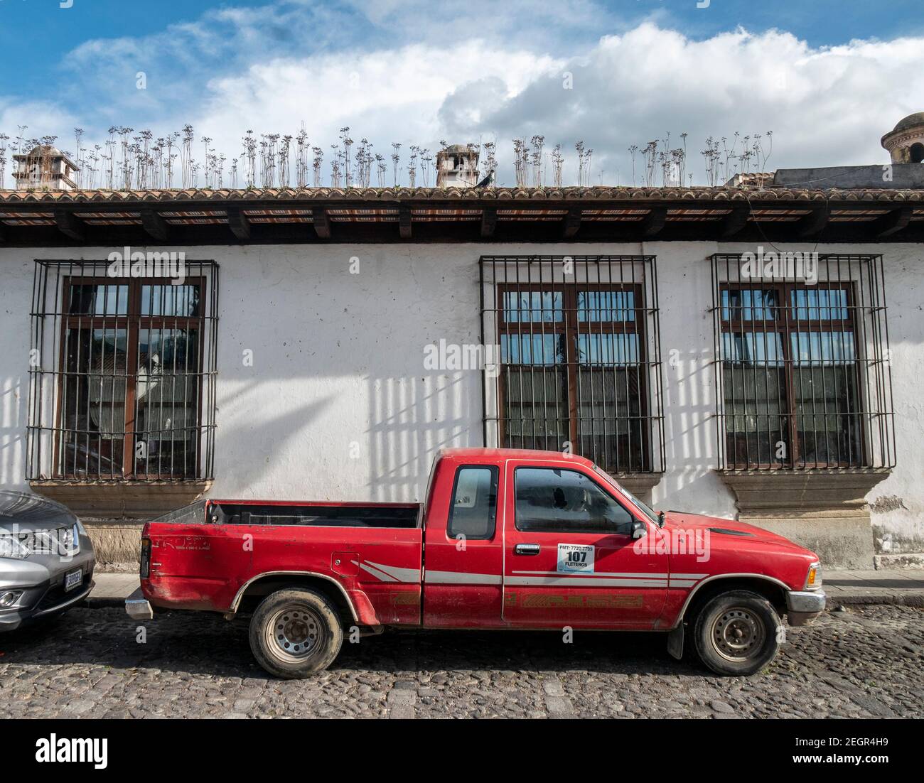 Guatemala, Antigua - May 26, 2019 - Old red pickup truck in front of colonial style house with rod iron bars on windows Stock Photo