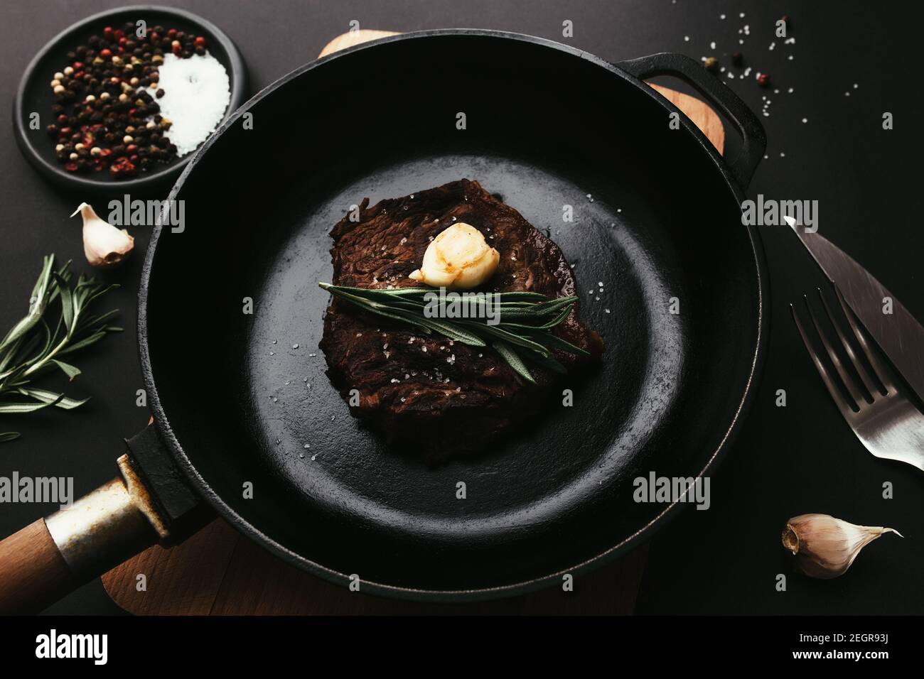 Ribeye steak on castiron pan, board with rosemary, garlic, knife, fork