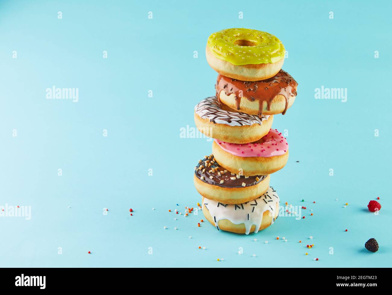 Multicolored donuts with icing and sprinkling stacked in a stack on a blue background. Stock Photo