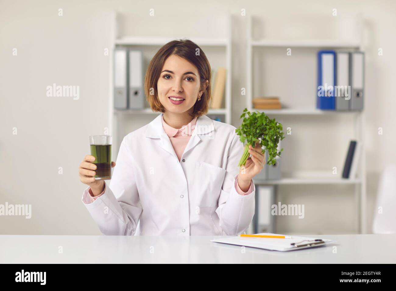 Dietitian sitting in clinic office, looking at camera and holding fresh detox parsley drink Stock Photo