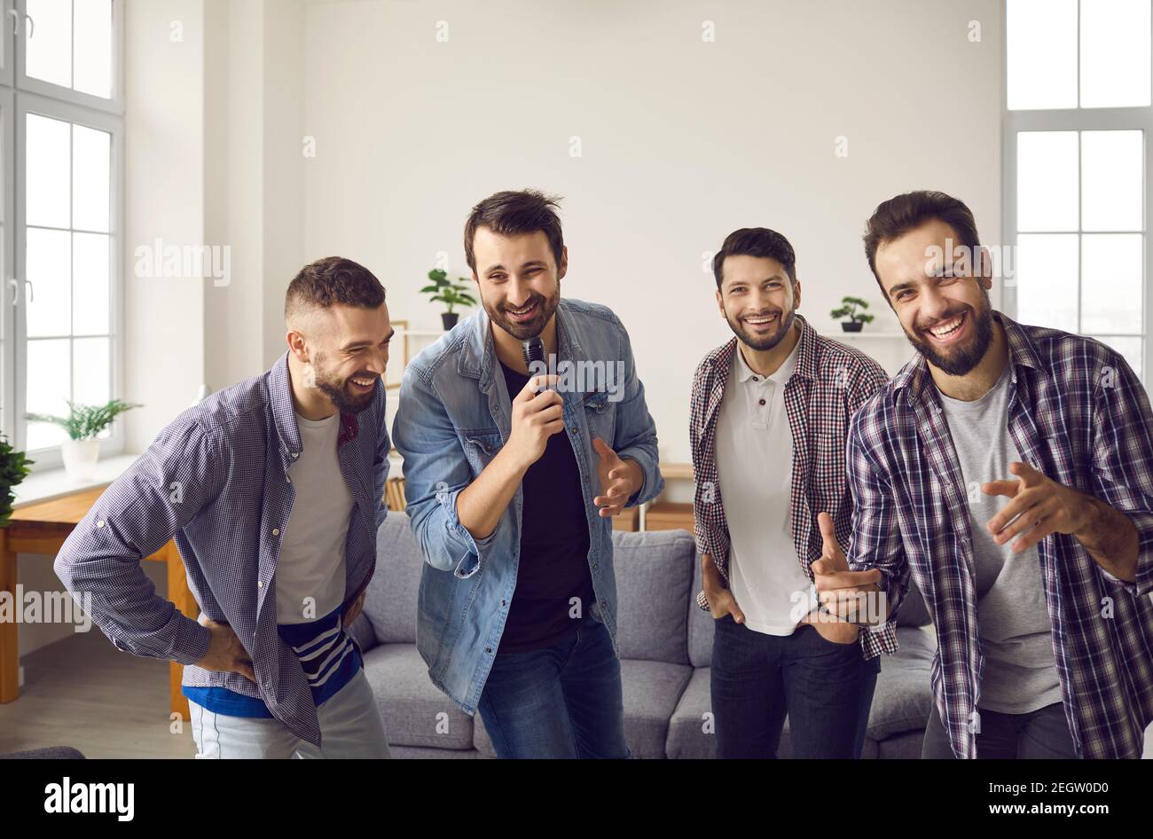 Positive cheerful male friends singing favourite songs on karaoke microphone together during home party Stock Photo